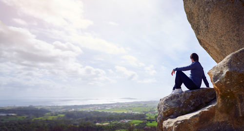 Full length of man sitting on rock against sky