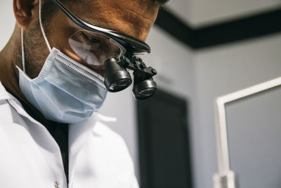 Male dentist wearing mask and surgical loupes while working in clinic