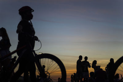 Silhouette people riding bicycle against sky during sunset