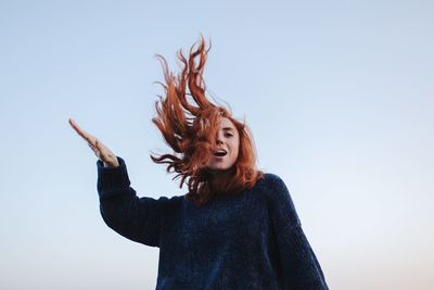 Low angle view of cheerful woman against clear sky