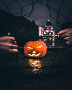Cropped hands breaking fence against illuminated jack o lantern in city at night