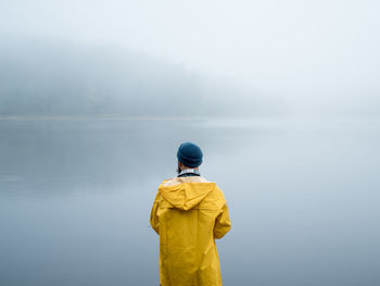 Rear view of man standing by foggy lake