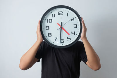 Midsection of woman holding alarm clock against white background