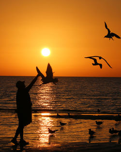 Silhouette man with arms outstretched on sea against sky during sunset