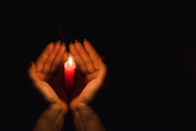 Close-up of hand by lit candle in darkroom