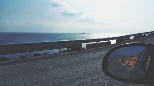 Close-up of side-view mirror by sea against sky
