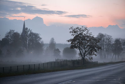 Road by trees against sky during sunset