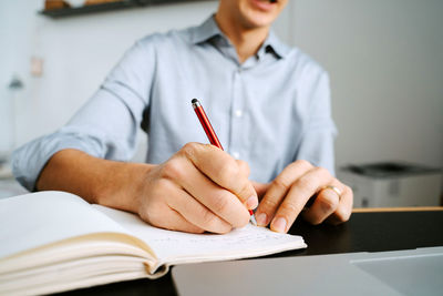 Unrecognizable crop male entrepreneur sitting at table and writing in notebook while planning business project
