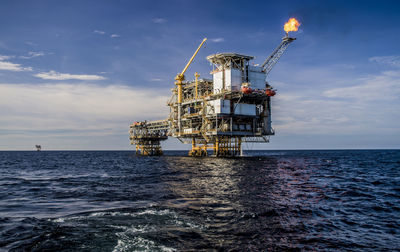 Offshore platform in sea against cloudy sky