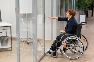 Red-haired caucasian woman in a wheelchair trying to open the door in the office