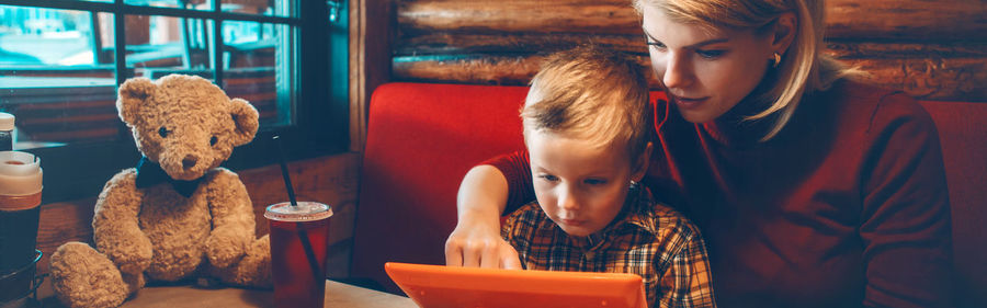 Caucasian mother and boy son choosing food meal from digital tablet touch pad menu at restaurant