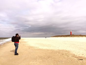 A man standing on the beach against the sky to photograph the lighthouse on texel