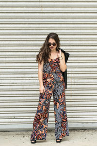 Confident female model wearing sunglasses while standing by closed shutter