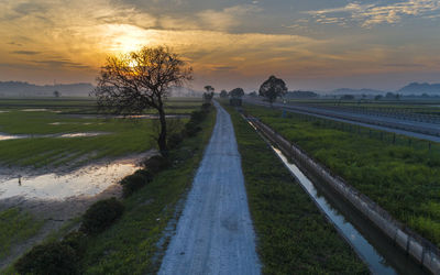 Road amidst field against sky during sunset