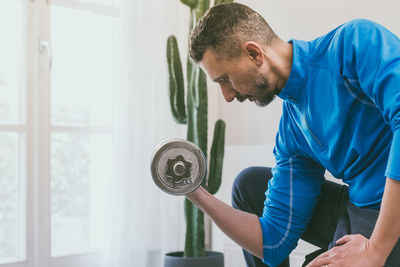 Sporty man working out and trains at home. fit boy doing exercises for biceps in the living room. 