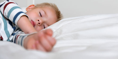 Sleeping child in bed. cute little kid sleeps on white blanket on its side, lying during day sleep