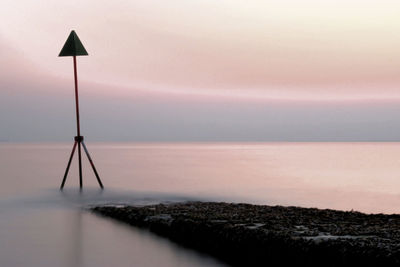 Marker in sea against sky during sunrise