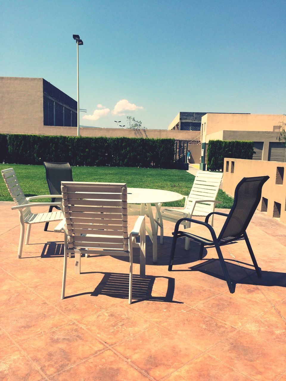 chair, table, empty, absence, building exterior, sunlight, built structure, architecture, bench, restaurant, seat, shadow, day, furniture, clear sky, sky, relaxation, outdoors, no people, sidewalk cafe