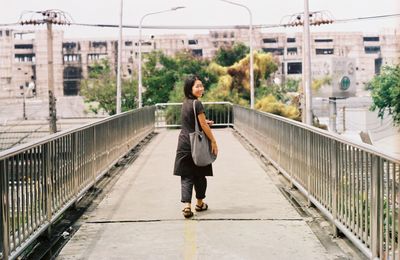 Woman walking on footbridge in city against sky