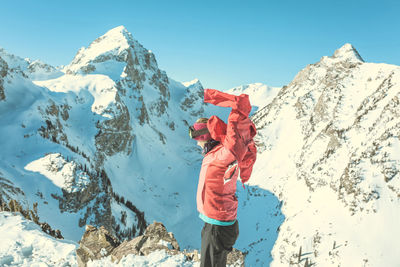 Side view of woman wearing jacket while standing against snowcapped mountain