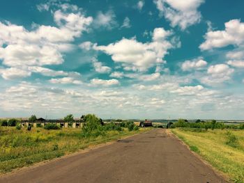 Road passing through field against cloudy sky