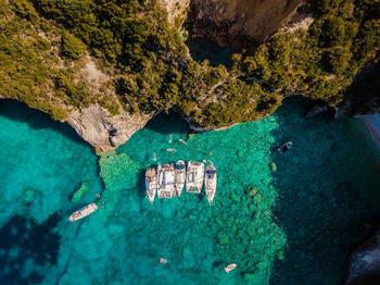 Anchored sailboats in turquise blue by near large sea caves in paxos island greece. 