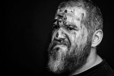 Close-up of man with paint on face looking away against black background