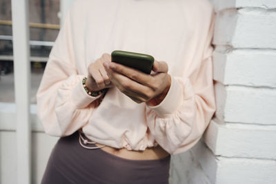 Woman using smart phone while leaning on brick wall