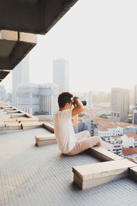 Side view of man sitting on buildings against clear sky