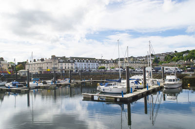 Boats moored at harbor against cloudy sky