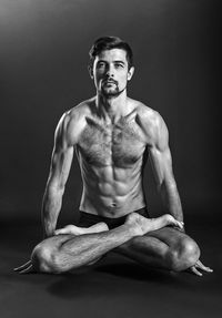 Portrait of young man sitting against black background