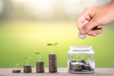 Close-up of hand holding coins in jar