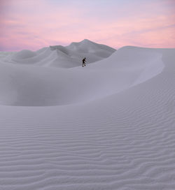 Man walking on desert against sky during sunset