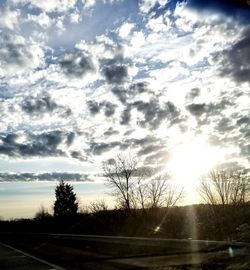 Road by silhouette trees against sky during sunset