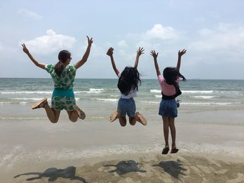Full length rear view of happy friends jumping at beach