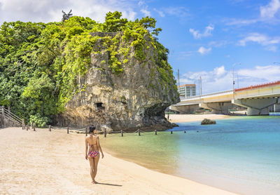 Young woman in swimsuit from behind on the sandy beach naminoue in naha city in okinawa, japan.