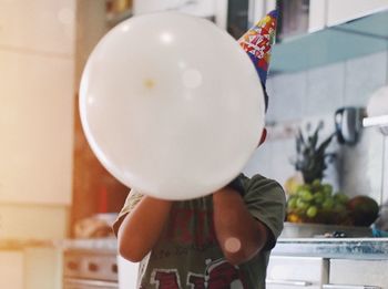 Rear view of boy holding balloons at home