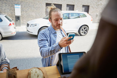 Young male customer paying through card reader at food truck in city