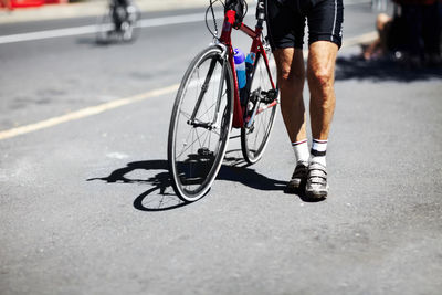 Low section of man walking with bicycle on road