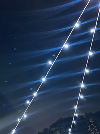 Low angle view of fairy lights streaming through blue sky at night