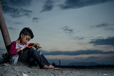 Surface level of boy studying by tree at dusk