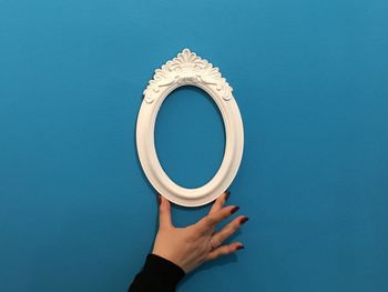 Cropped hand of woman holding picture frame against blue background