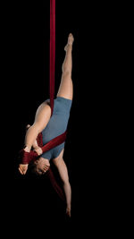 Young woman hanging on fabric while dancing against black background