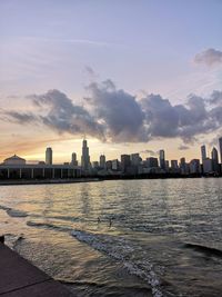 Sea by buildings against sky during sunset