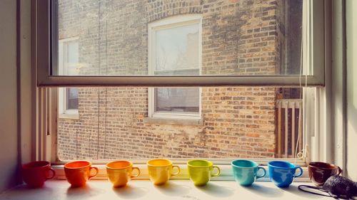 Colorful mugs on window sill in apartment