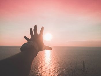 Cropped hand reaching sun at beach