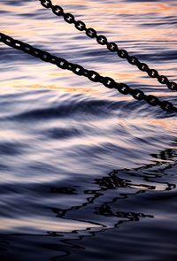 Close-up of chain on water against sky during sunset