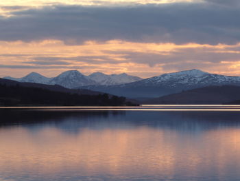 Scenic view of lake and snowcapped mountains against cloudy sky during sunset