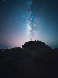 Back view of unrecognizable traveler male standing on hill while admiring spectacular scenery of milky way over mountainous in starry night