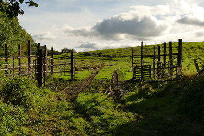 Fence on grassy field against cloudy sky